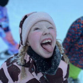 Happy young girl wearing a pink beanie and jacket sticking her tongue out while playing in the snow.