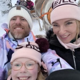 Happy family taking a selfie on a reindeer sleigh ride through a snowy winter landscape.