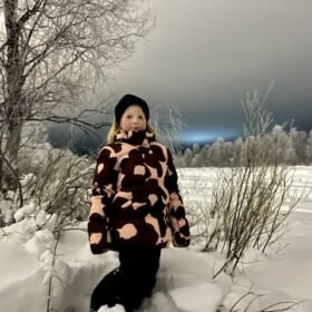 Young girl in a patterned winter jacket standing outdoors in deep snow surrounded by frosty trees.
