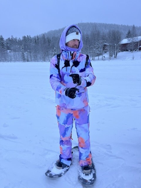 Person wearing a colorful purple ski suit and snowshoes standing in a snowy winter landscape.
