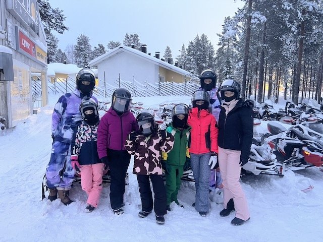 Family in colorful winter suits and helmets posing in the snow before a snowmobile safari.