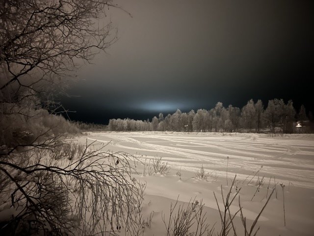Frozen snow-covered river landscape at night with frosted trees and winter tracks under a dark sky.
