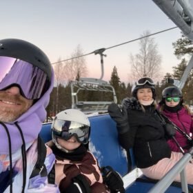 Family wearing helmets and goggles taking a selfie on a ski chairlift during a winter vacation.