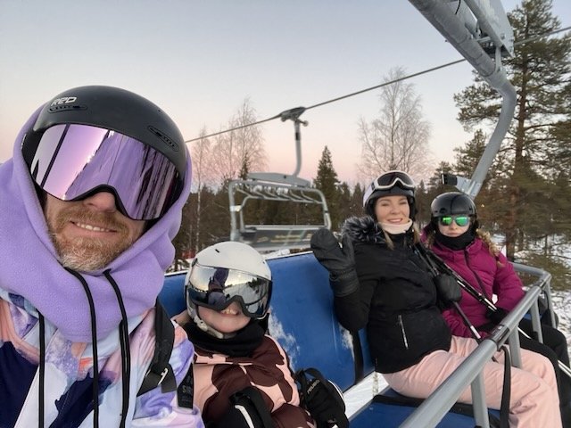 Family wearing helmets and goggles taking a selfie on a ski chairlift during a winter vacation.