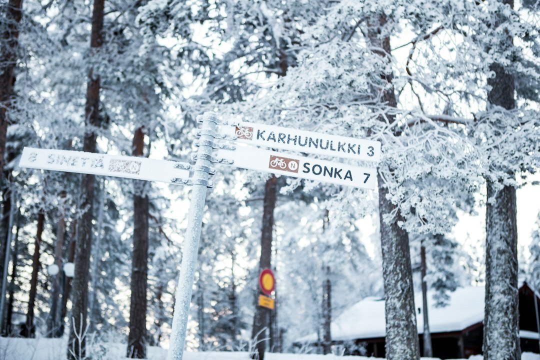 Snow-covered directional trail sign pointing to Karhunulkki and Sonka in a frosty winter forest.